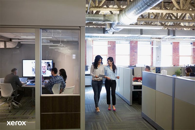 Due donne camminano in un moderno ufficio open space, impegnate in una conversazione e circondate da postazioni di lavoro. Due donne camminano in un moderno ufficio open space, impegnate in una conversazione e circondate da postazioni di lavoro.