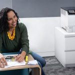 Stampante Xerox® VersaLink® C620 in un ufficio Donna sorridente in un ufficio accanto alla stampante a colori Xerox® VersaLink® C620