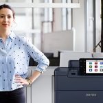 Una donna in piedi accanto alla stampante Xerox® PrimeLink® Serie C9200 in un ufficio moderno Una donna in piedi accanto alla stampante Xerox® PrimeLink® Serie C9200 in un ufficio moderno